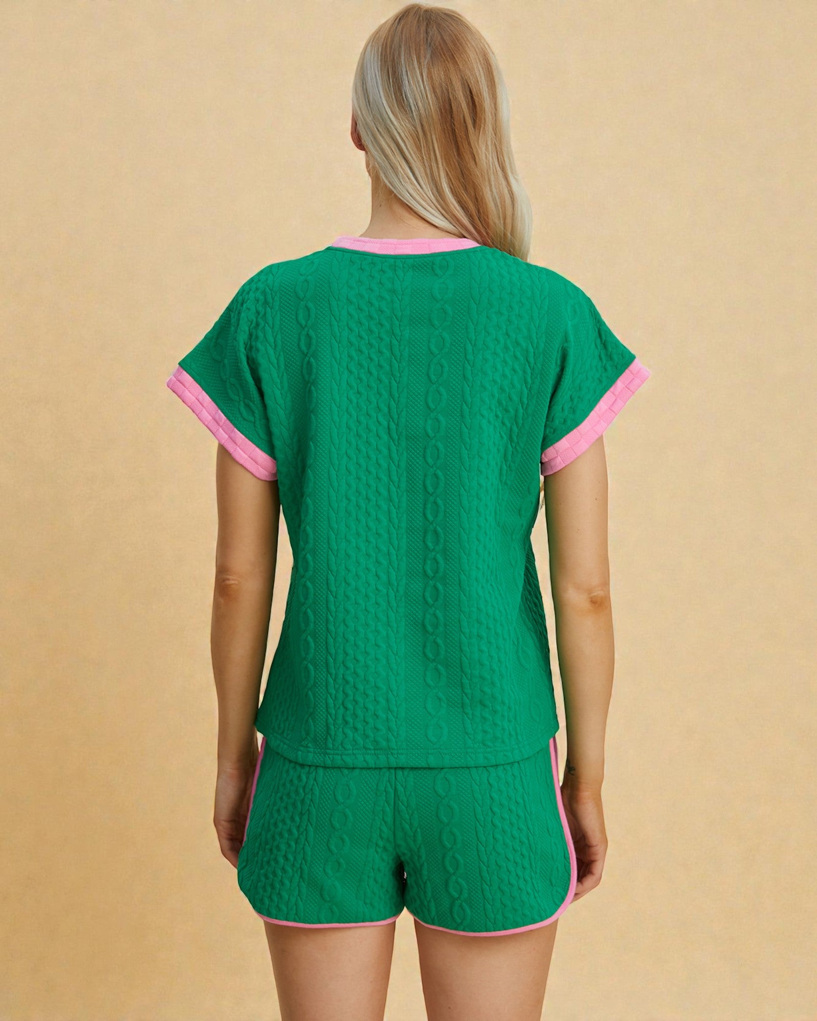 Green pajama set with pink trim worn by a person on a beige background