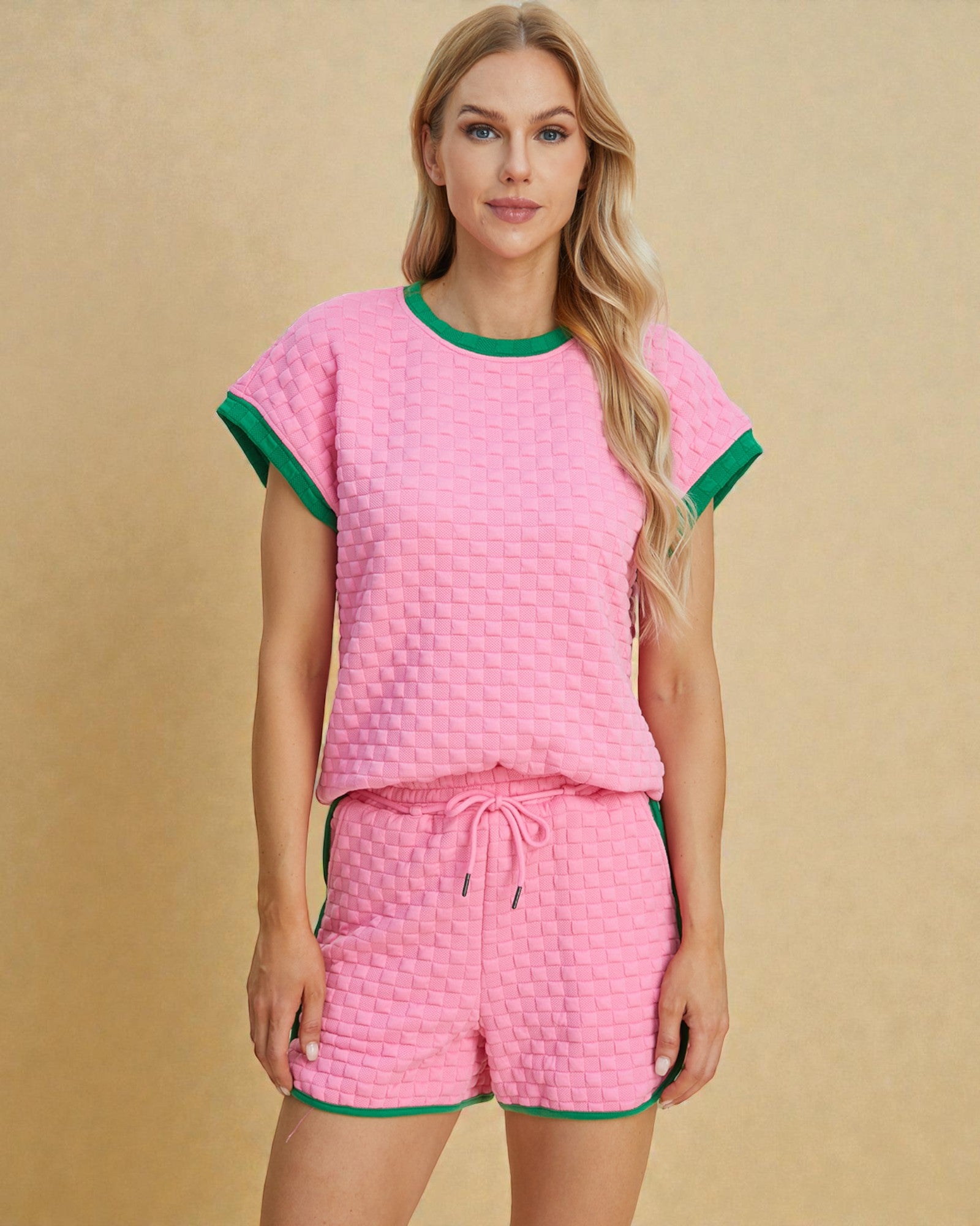 Woman wearing a pink textured pajama set with green trim on a beige background