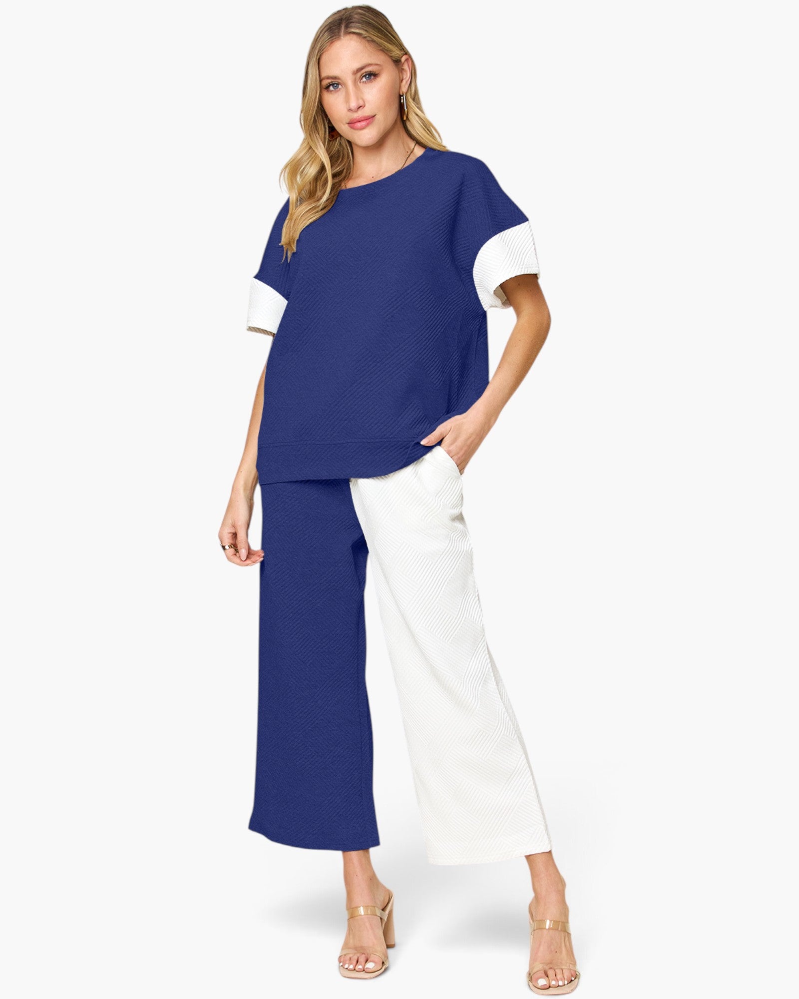 A woman modeling a color-blocked short-sleeve top and matching wide-leg pants set. The top has a navy blue body with white sleeves, and the pants are split down the middle with navy on one leg and white on the other.