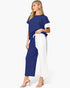 A woman modeling a color-blocked two-piece outfit consisting of a navy blue short-sleeve top with white sleeve panels and matching navy wide-leg pants with white side panels, paired with nude heeled sandals against a light gray background.