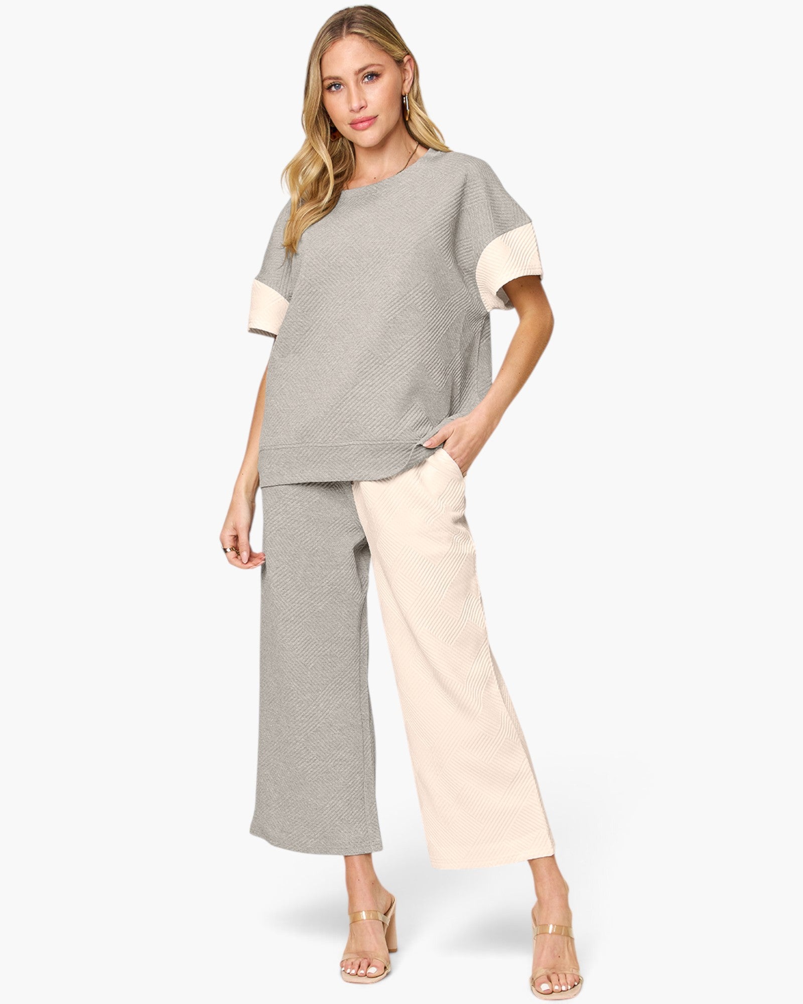 A woman modeling a two-piece color-blocked knit set featuring a short-sleeve top with gray and cream color blocking, and matching wide-leg cropped pants.