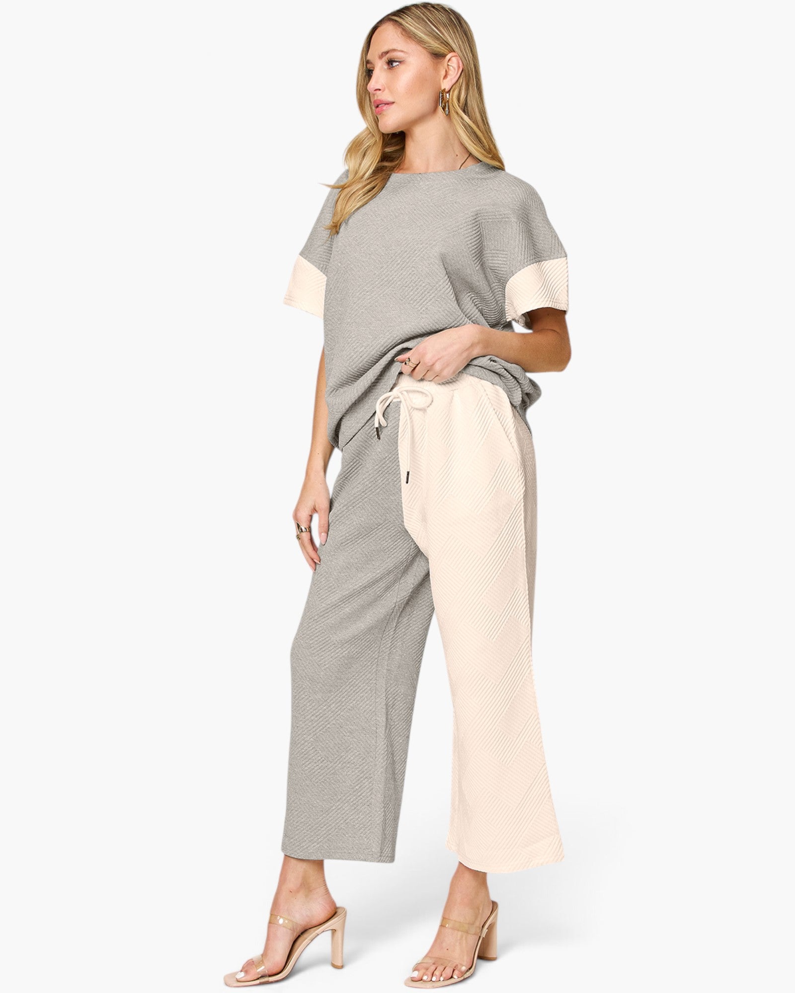 A woman modeling a two-piece knit loungewear set featuring a short-sleeve top with color-blocked cream sleeves and matching wide-leg cropped pants with a cream side pocket, set against a plain light gray background.
