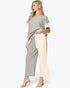 A woman modeling a two-piece knit loungewear set featuring a short-sleeve top with color-blocked cream sleeves and matching wide-leg cropped pants with a cream side pocket, set against a plain light gray background.