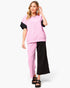 A woman modeling a color-blocked lounge set consisting of a short-sleeve sweatshirt and matching pants in pink and black, paired with black sandals against a light gray background.