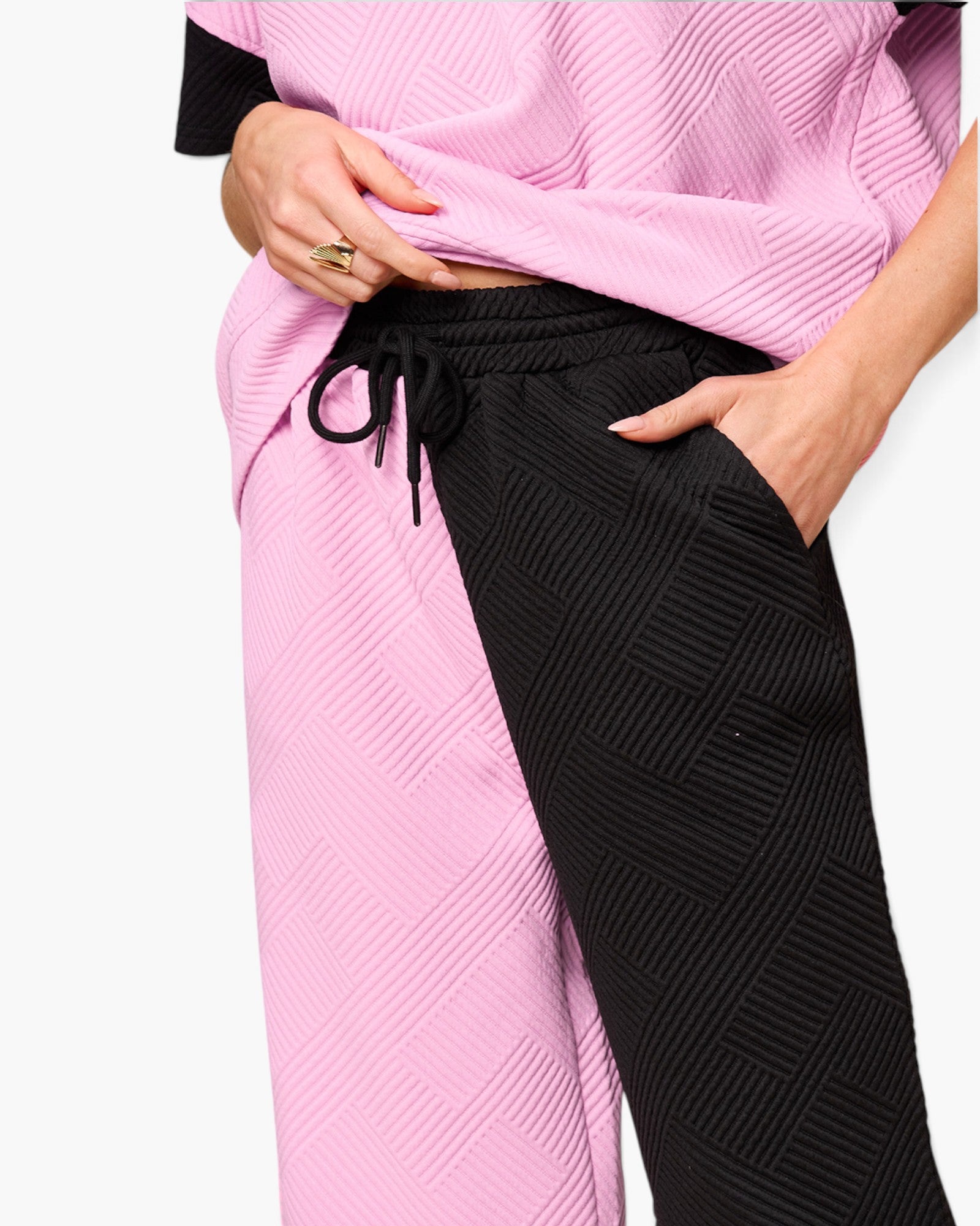 Close-up of a person wearing textured two-tone pants with one leg in light pink and the other in black, paired with a matching pink top against a light gray background.