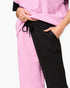 Close-up of a person wearing textured two-tone pants with one leg in light pink and the other in black, paired with a matching pink top against a light gray background.