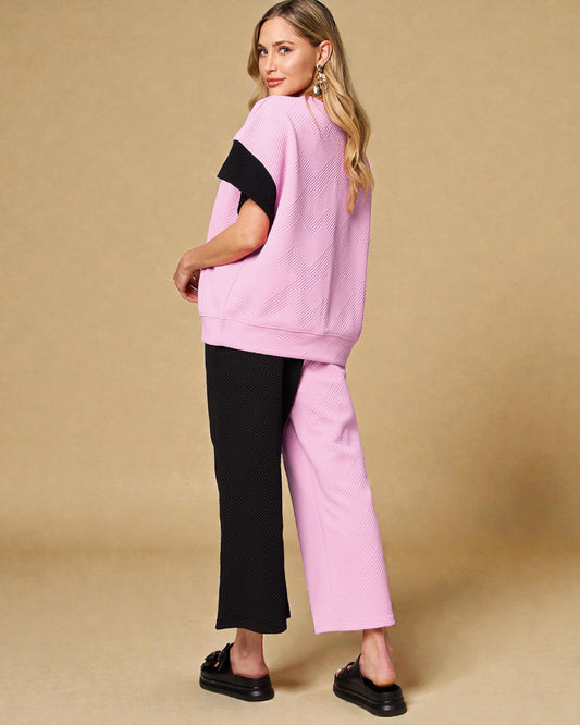 Woman wearing a pink outfit with black sleeves and pants on a beige background