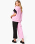 A woman modeling a color-blocked knit set consisting of a light pink short-sleeve top with a black sleeve and matching light pink wide-leg pants, shown from a three-quarters back view against a plain white background.