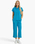 A woman modeling a matching bright turquoise blue loungewear set consisting of a short-sleeve cropped hoodie and wide-leg cropped pants, paired with white sneakers against a clean white studio background.