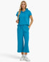 A woman modeling a matching bright turquoise blue loungewear set consisting of a short-sleeve hooded top and wide-leg cropped pants, paired with white sneakers against a plain white studio background.