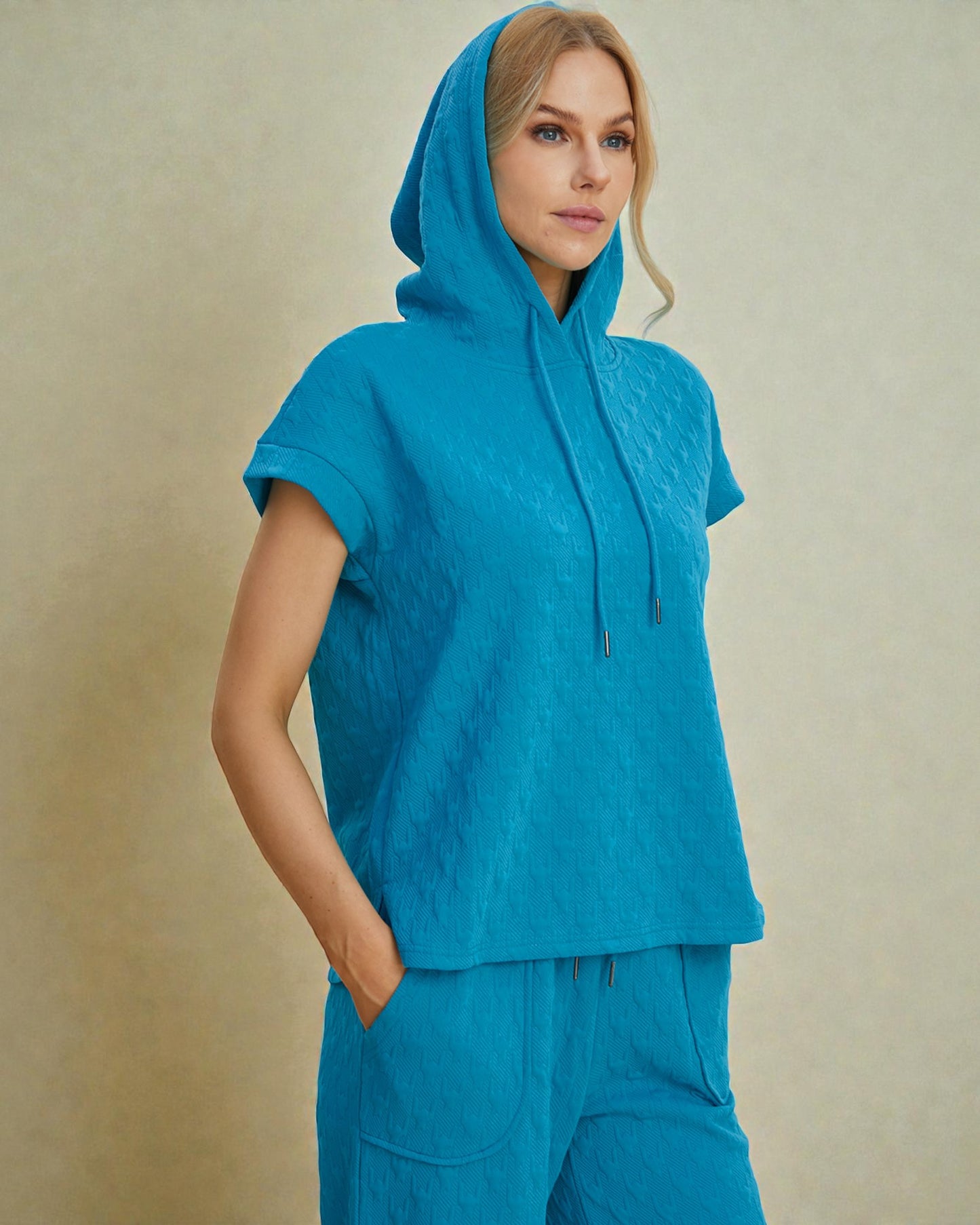 Woman wearing a blue hooded top and pants against a beige background