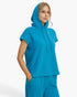 A woman wearing a bright turquoise blue hooded short-sleeve top and matching pants, photographed against a clean light gray studio background.