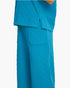 A close-up of a person wearing bright turquoise-blue textured scrub-style pants and a matching top against a plain light gray background.