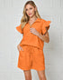 Woman wearing an orange outfit with a white tiled background