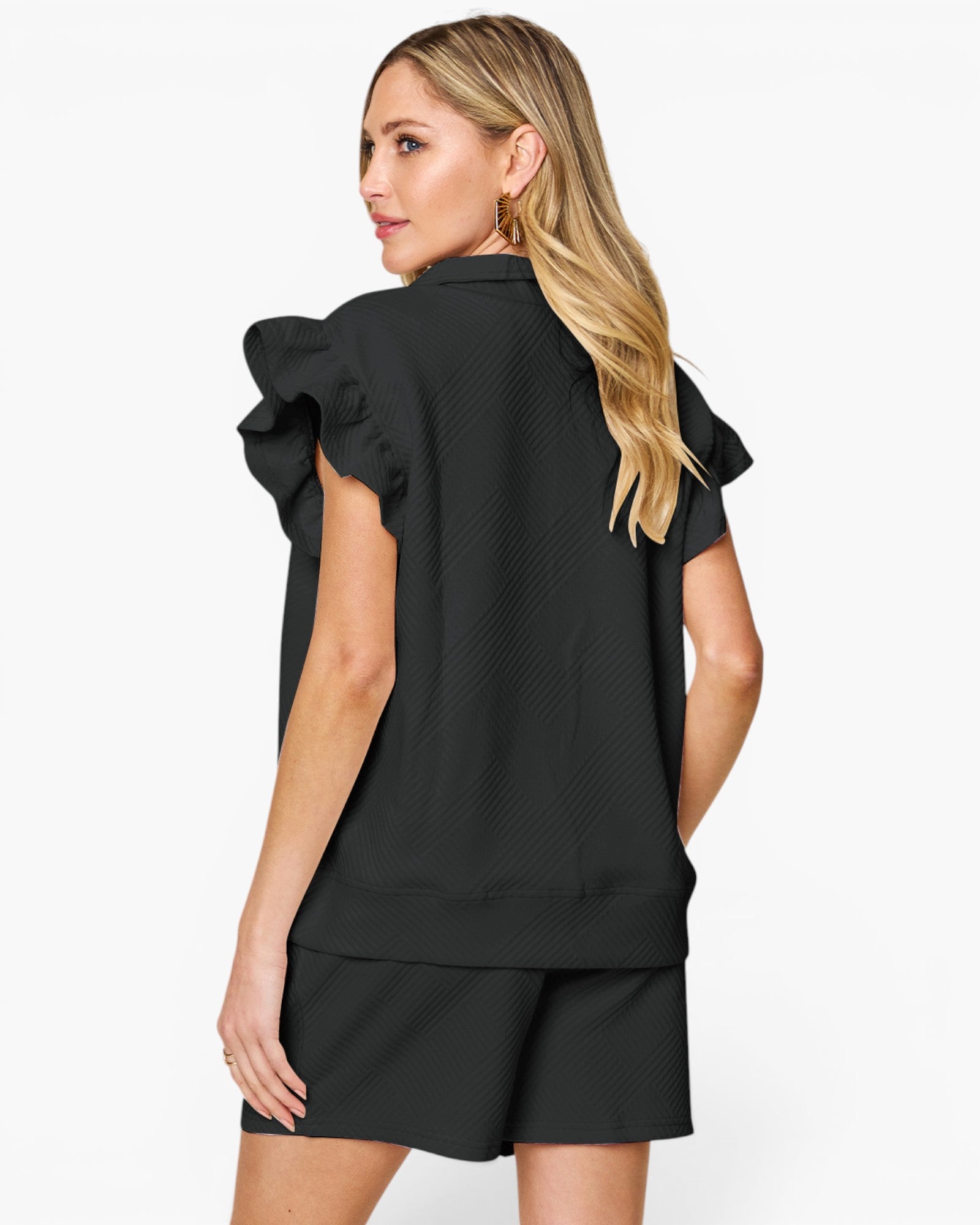 A woman shown from the back wearing a black textured short-sleeve top with dramatic ruffled shoulder details and matching black shorts, against a plain light gray studio background.