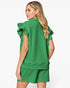 A woman shown from the back wearing a bright green short-sleeve top with dramatic ruffled shoulders and matching green shorts against a plain light gray studio background.