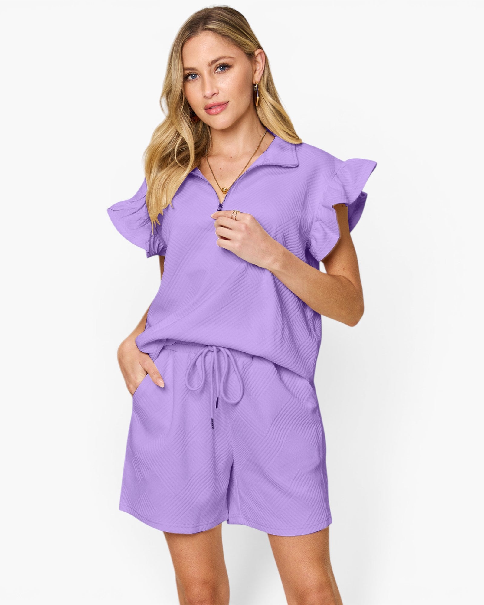 A woman modeling a lavender purple two-piece matching set featuring a short-sleeve collared top with ruffled sleeves and matching drawstring shorts, set against a plain white studio background.