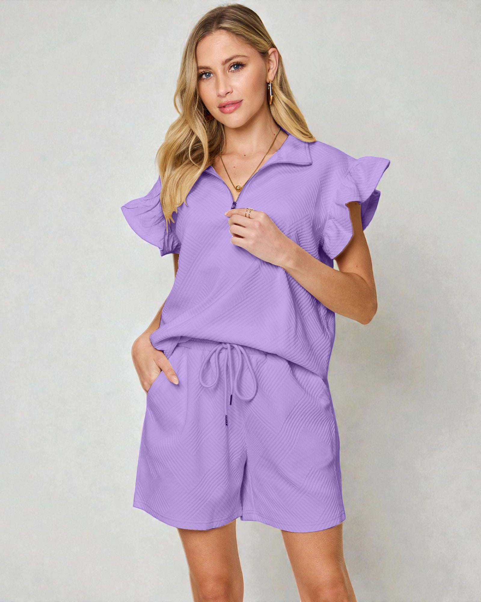 Woman wearing a purple outfit with ruffled sleeves on a plain background