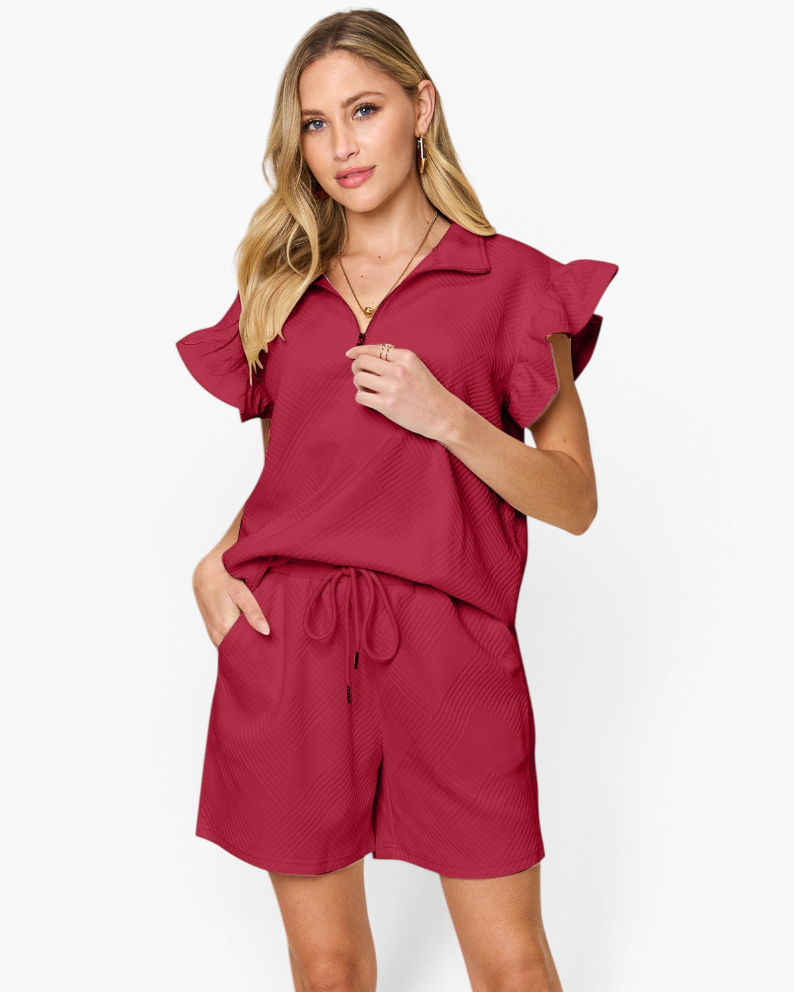 A woman modeling a matching two-piece set consisting of a short-sleeve collared top with ruffled sleeves and matching drawstring shorts, in a deep berry red color, against a plain white studio background.