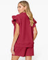 A woman shown from the back wearing a matching burgundy two-piece set consisting of a short-sleeve top with dramatic ruffled shoulder details and matching shorts, against a plain white studio background.