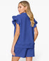 A woman shown from the back wearing a matching royal blue textured top and shorts set, featuring ruffled short sleeves on the top, against a plain white studio background.