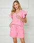 Woman wearing a pink outfit with ruffled sleeves against a white background