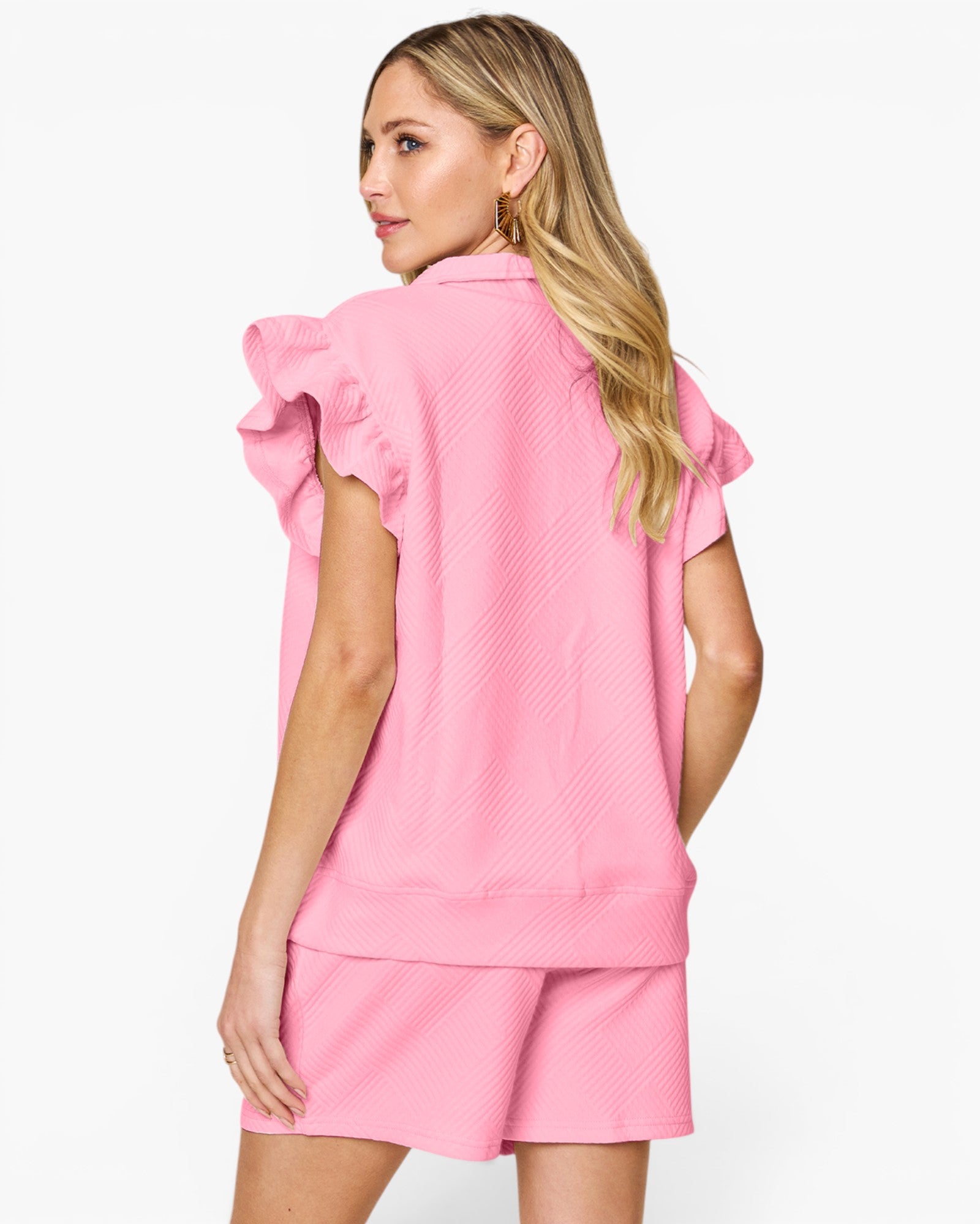 A woman shown from the back wearing a bright pink matching set consisting of a short-sleeve top with ruffled sleeves and matching shorts, against a plain beige studio background.