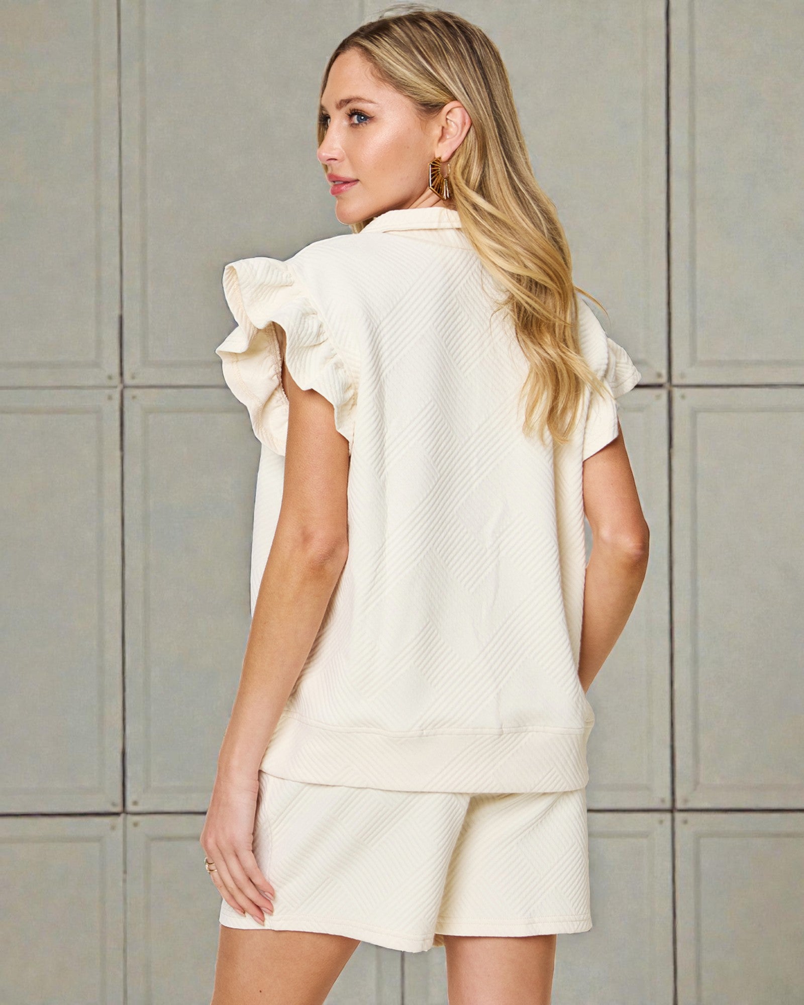 Woman wearing a cream-colored outfit with ruffled sleeves against a neutral background