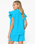 A woman shown from the back wearing a bright turquoise blue matching set consisting of a short-sleeve top with dramatic ruffled shoulders and matching shorts, against a plain white studio background.