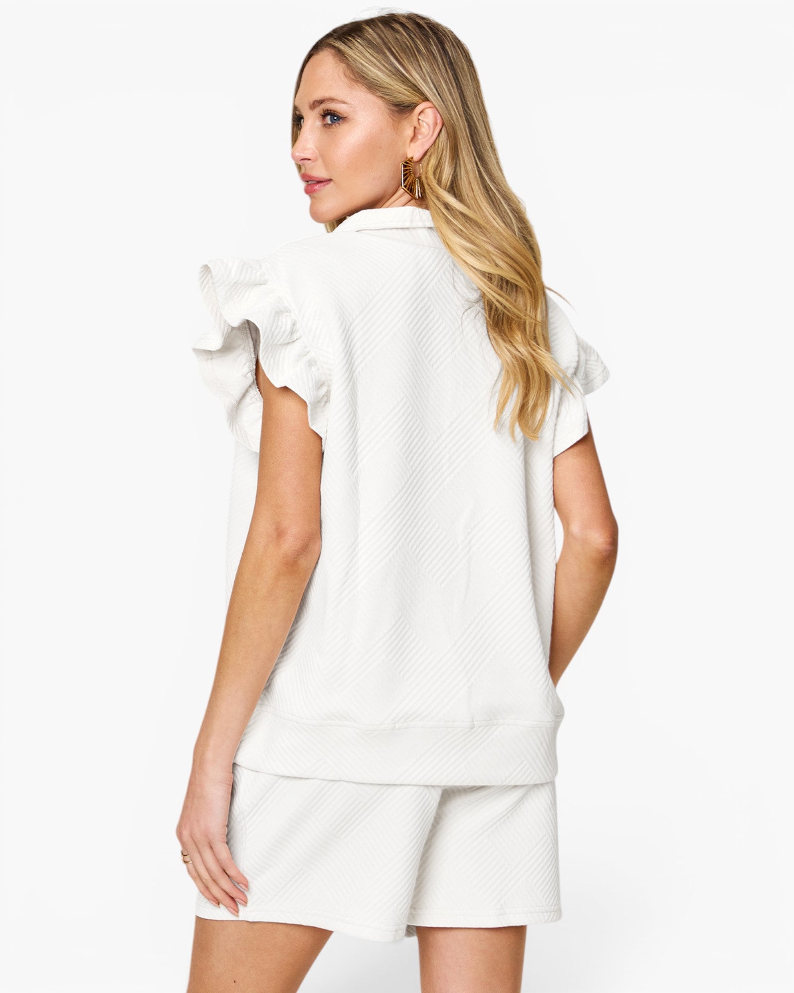 A woman shown from the back wearing a white textured short-sleeve top with ruffled sleeves and matching white shorts against a plain white studio background.