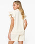 A woman shown from the back wearing a cream-colored textured short-sleeve top with ruffled shoulder details and matching shorts against a plain white studio background.
