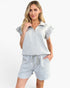 A woman modeling a light blue and white textured two-piece lounge set consisting of a short-sleeve collared top and matching drawstring shorts, set against a plain white studio background.