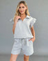 Woman wearing a light gray outfit with a top and shorts on a gray background