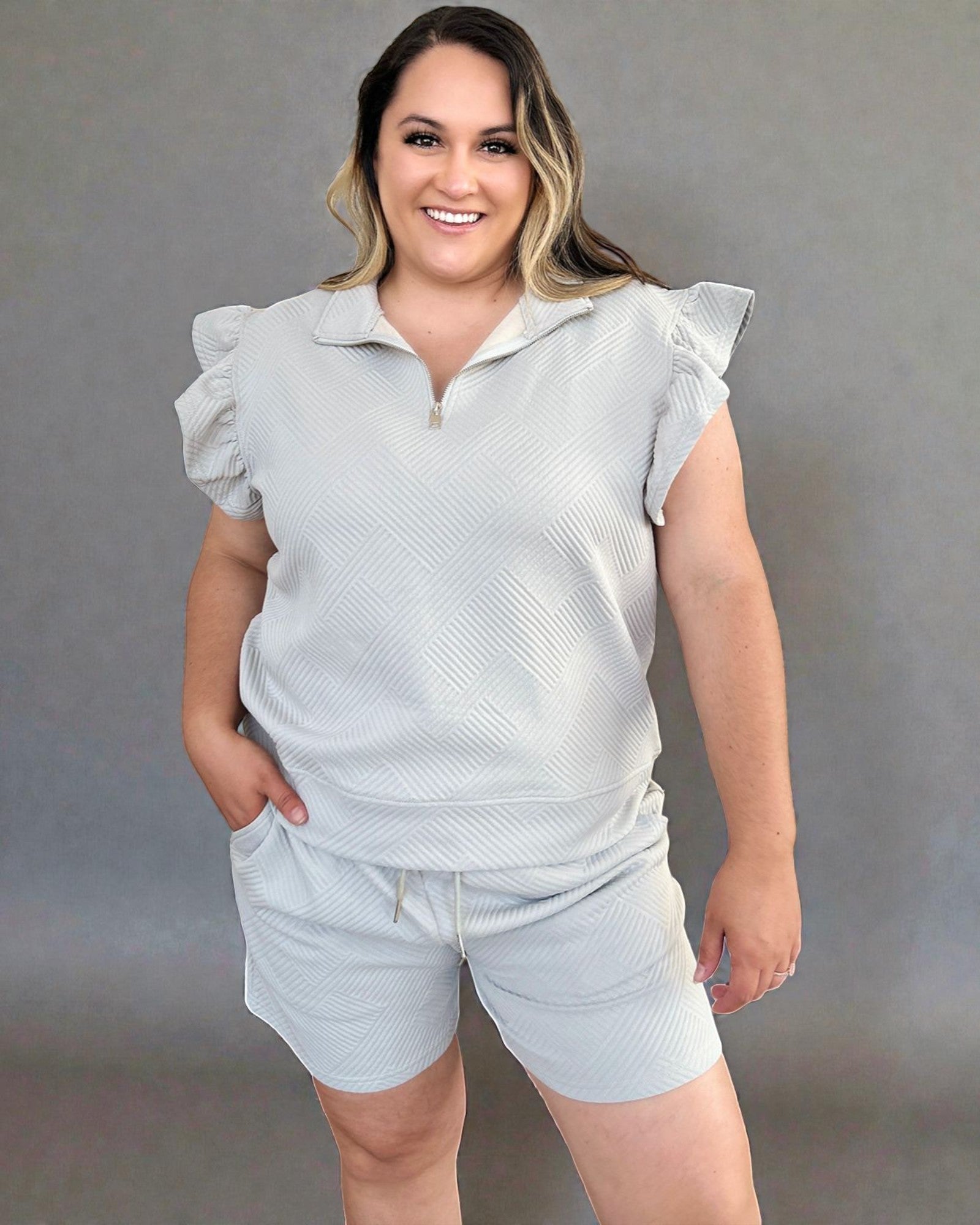 Woman wearing a light gray sleeveless top and shorts against a plain background