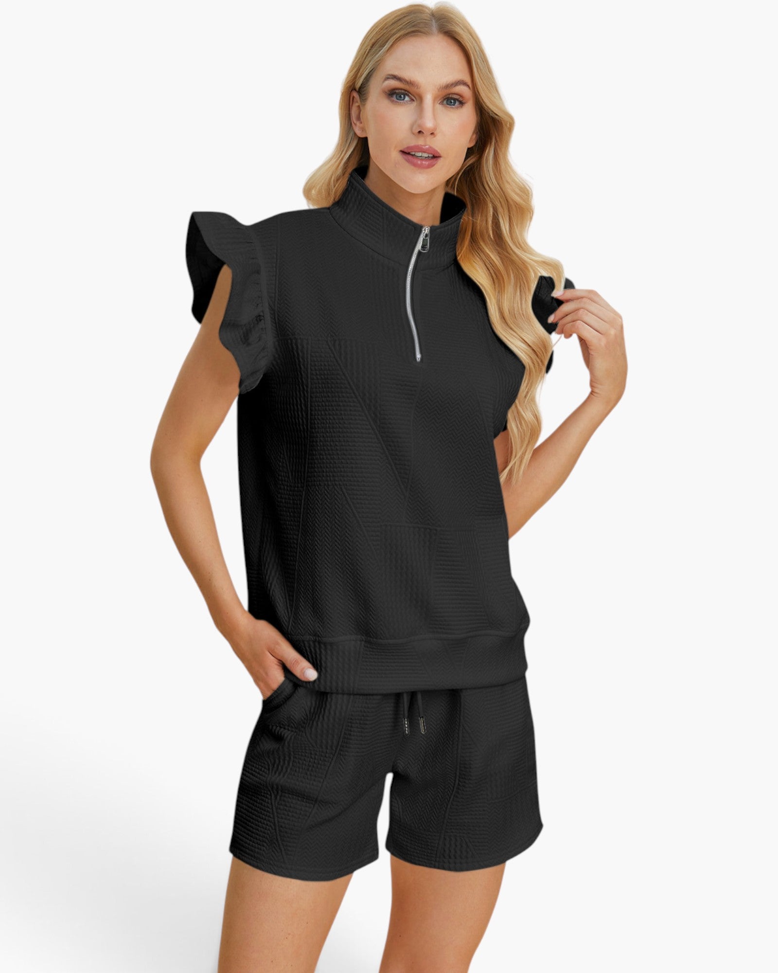 A woman modeling a black textured two-piece lounge set consisting of a short-sleeve quarter-zip top with ruffled sleeves and matching drawstring shorts, against a plain white studio background.