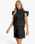 A blonde model wearing a black ribbed knit two-piece set consisting of a mock-neck short-sleeve top with a half-zip and ruffled sleeves, paired with matching drawstring shorts, against a plain white background.