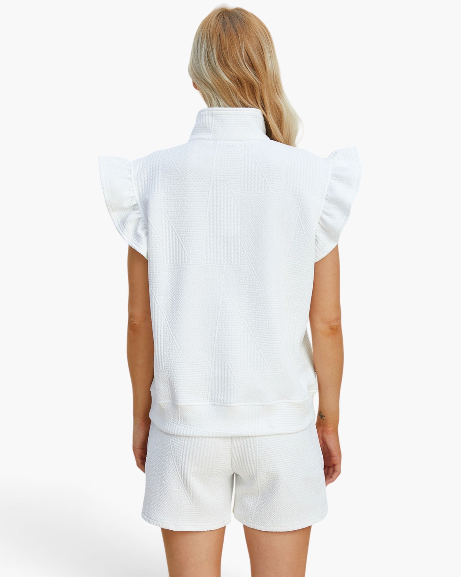 A woman shown from the back wearing a white sleeveless textured top with ruffled shoulders and matching white textured shorts against a plain white studio background.