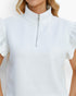 A close-up of a woman wearing a white textured short-sleeve top with a mock neck and a silver zipper at the collar.