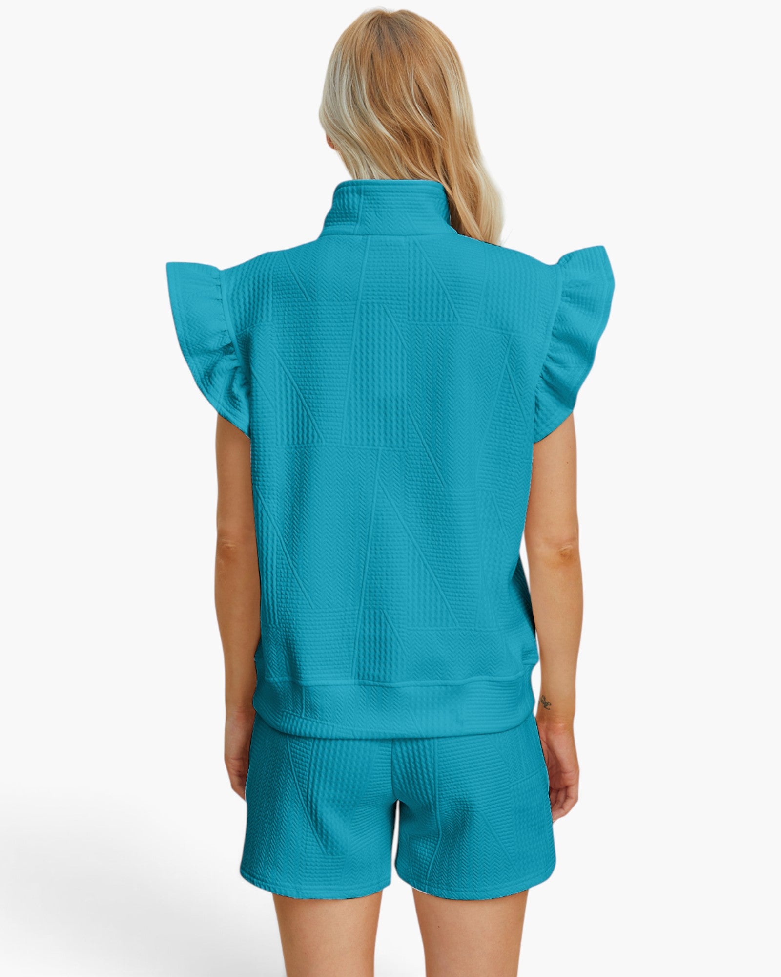 A woman shown from the back wearing a matching turquoise ribbed knit two-piece set with a sleeveless mock-neck top featuring ruffled shoulders and coordinating shorts, against a plain white studio background.