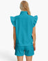 A woman shown from the back wearing a matching turquoise ribbed knit two-piece set with a sleeveless mock-neck top featuring ruffled shoulders and coordinating shorts, against a plain white studio background.