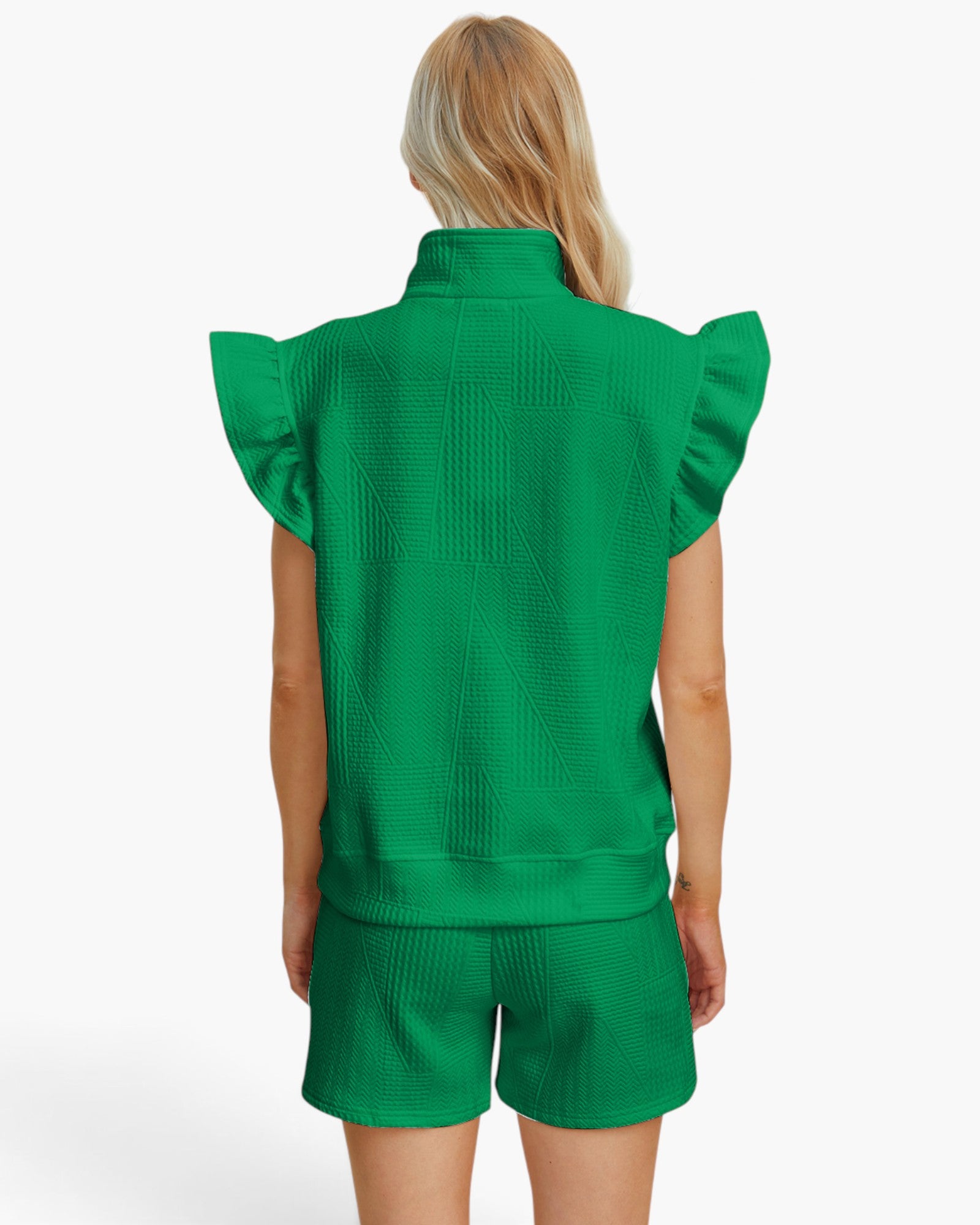 A model shown from the back wearing a bright green textured knit matching set consisting of a sleeveless mock-neck top with ruffled shoulders and matching shorts, against a plain white studio background.