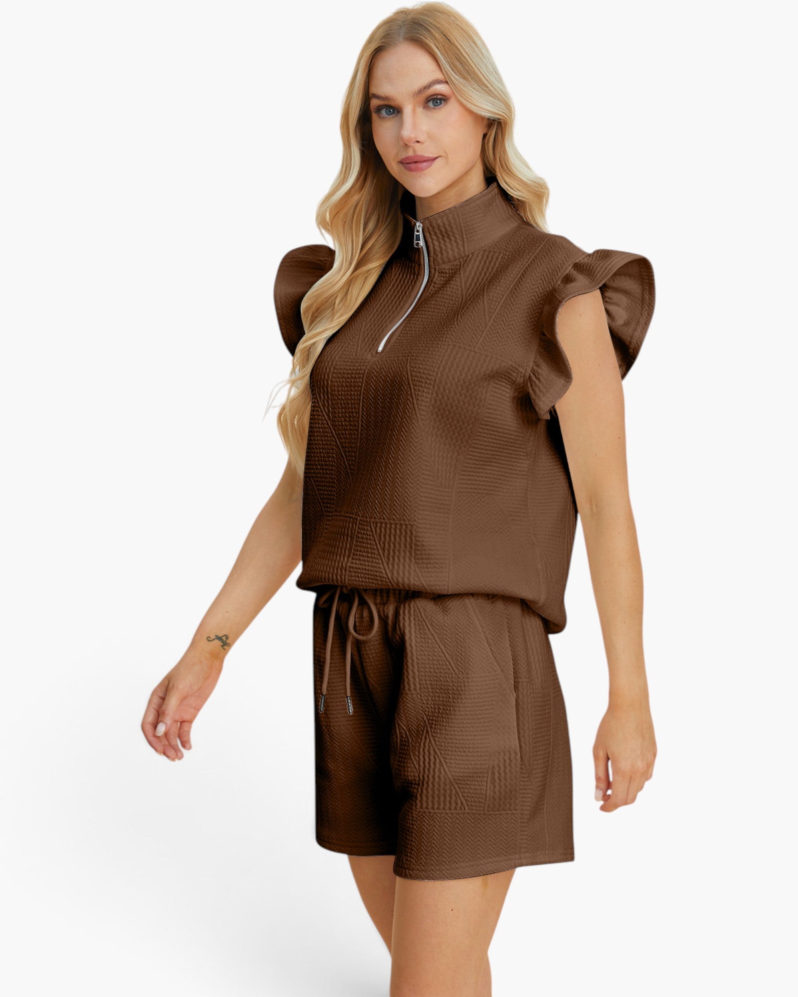 A woman modeling a brown textured two-piece set consisting of a sleeveless mock-neck top with a half-zip and ruffled shoulders, paired with matching drawstring shorts, against a plain white background.