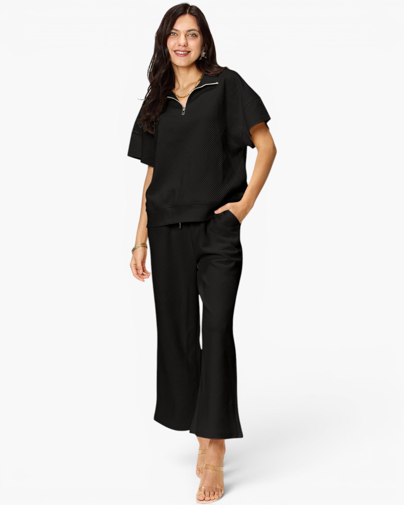 A woman modeling a black short-sleeve scrub top with a half-zip neckline and matching black scrub pants against a plain white background.