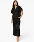 A woman modeling a black short-sleeve scrub top with a half-zip neckline and matching black scrub pants against a plain white background.