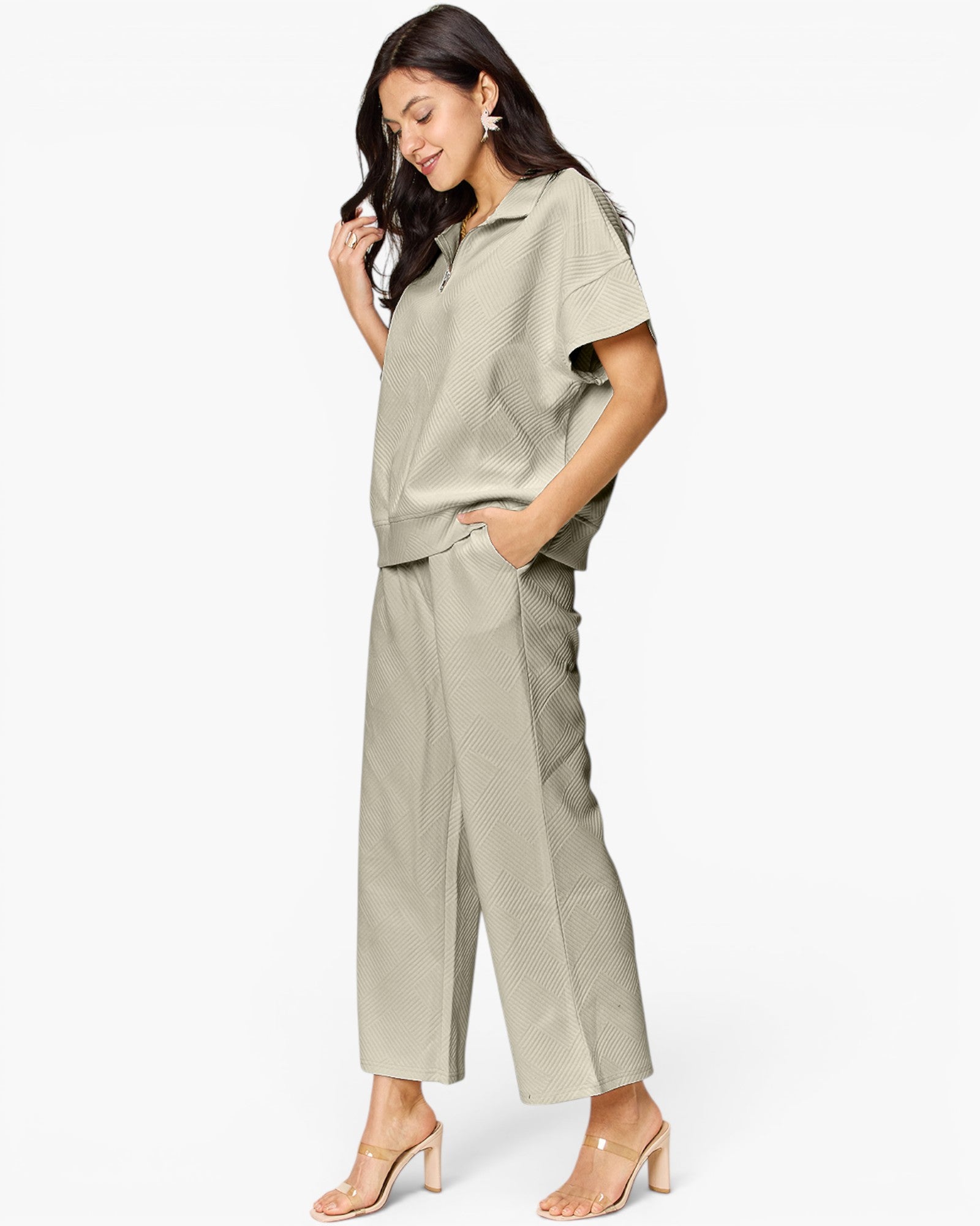 A woman modeling a matching light sage green two-piece set consisting of a short-sleeve collared top and wide-leg cropped trousers, paired with clear-strap heeled sandals against a plain white background.