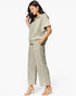 A woman modeling a matching light sage green two-piece set consisting of a short-sleeve collared top and wide-leg cropped trousers, paired with clear-strap heeled sandals against a plain white background.
