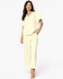 A woman modeling a light cream two-piece lounge set consisting of a short-sleeve collared top and matching wide-leg pants, set against a plain white studio background.