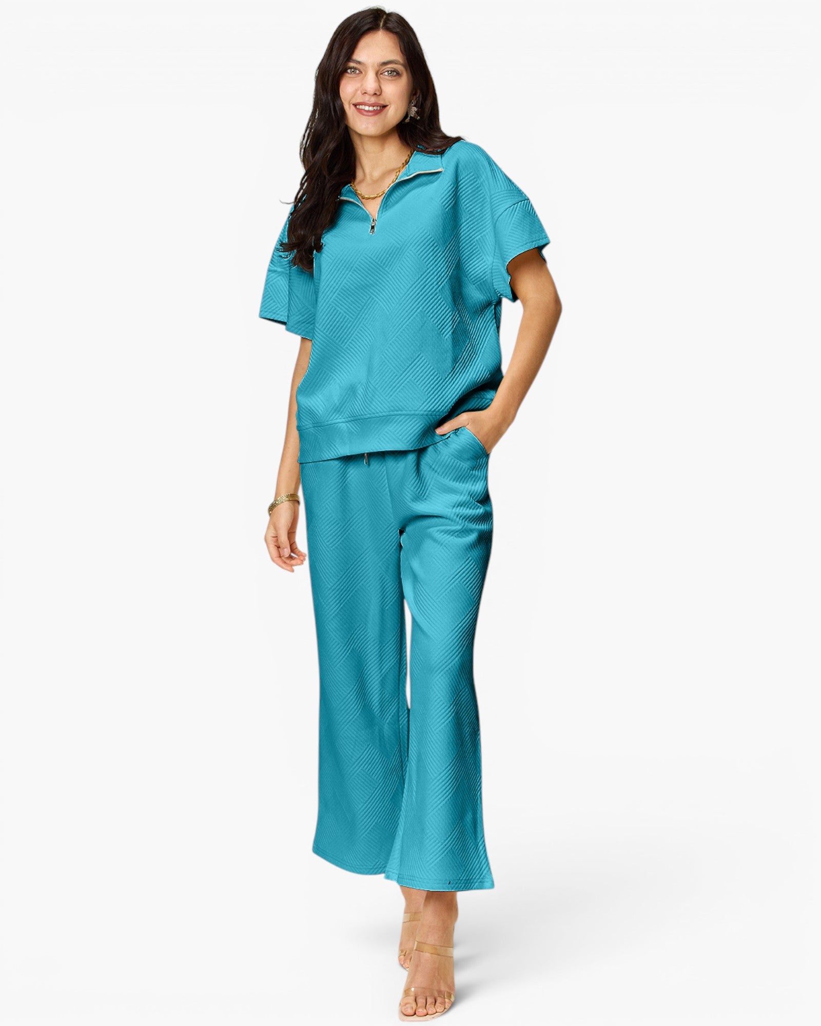 A woman modeling a matching turquoise blue lounge set consisting of a short-sleeve collared top and wide-leg pants, photographed against a clean white studio background.