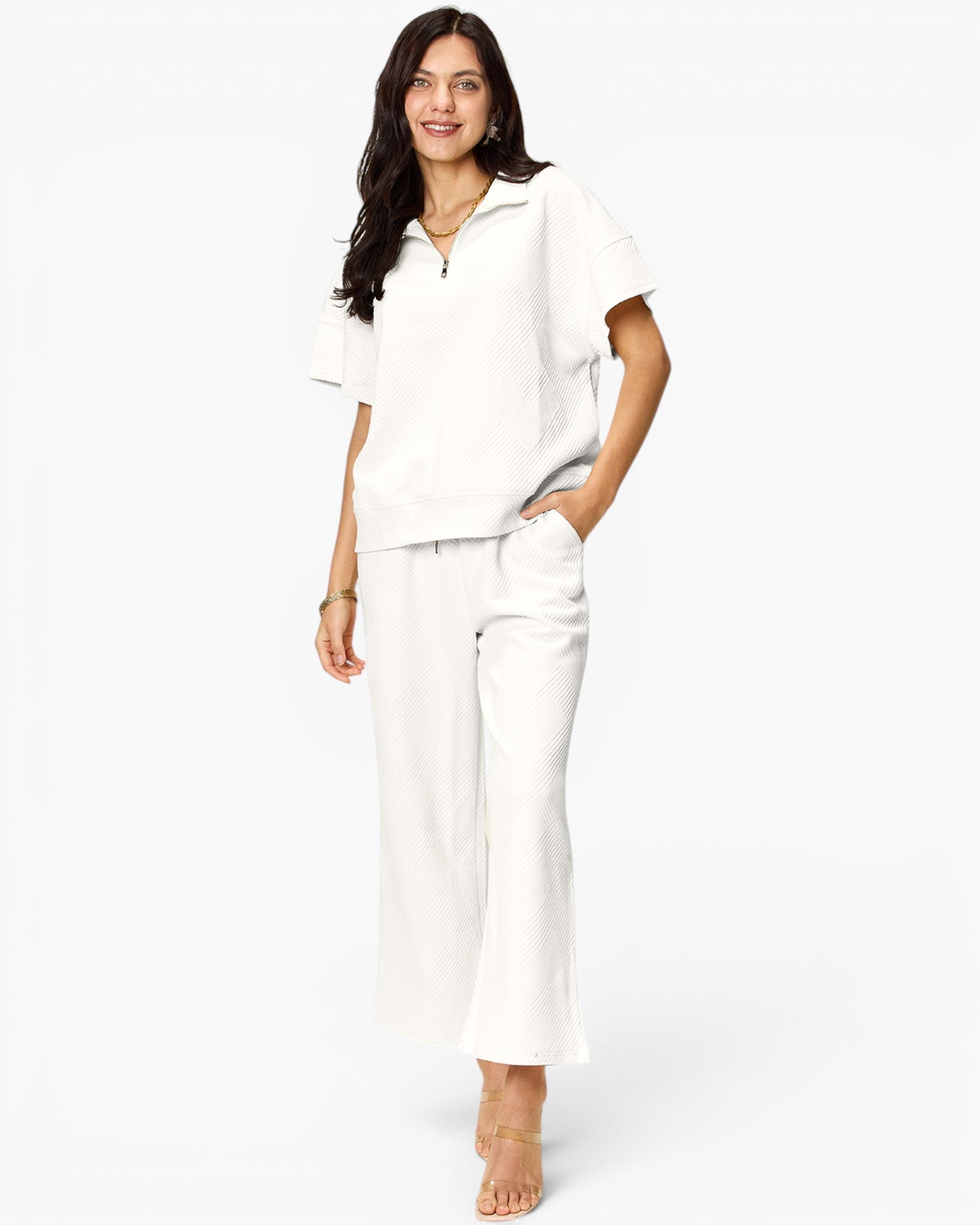 A woman modeling a matching white two-piece lounge set consisting of a short-sleeve half-zip polo shirt and wide-leg cropped pants, set against a plain white studio background.