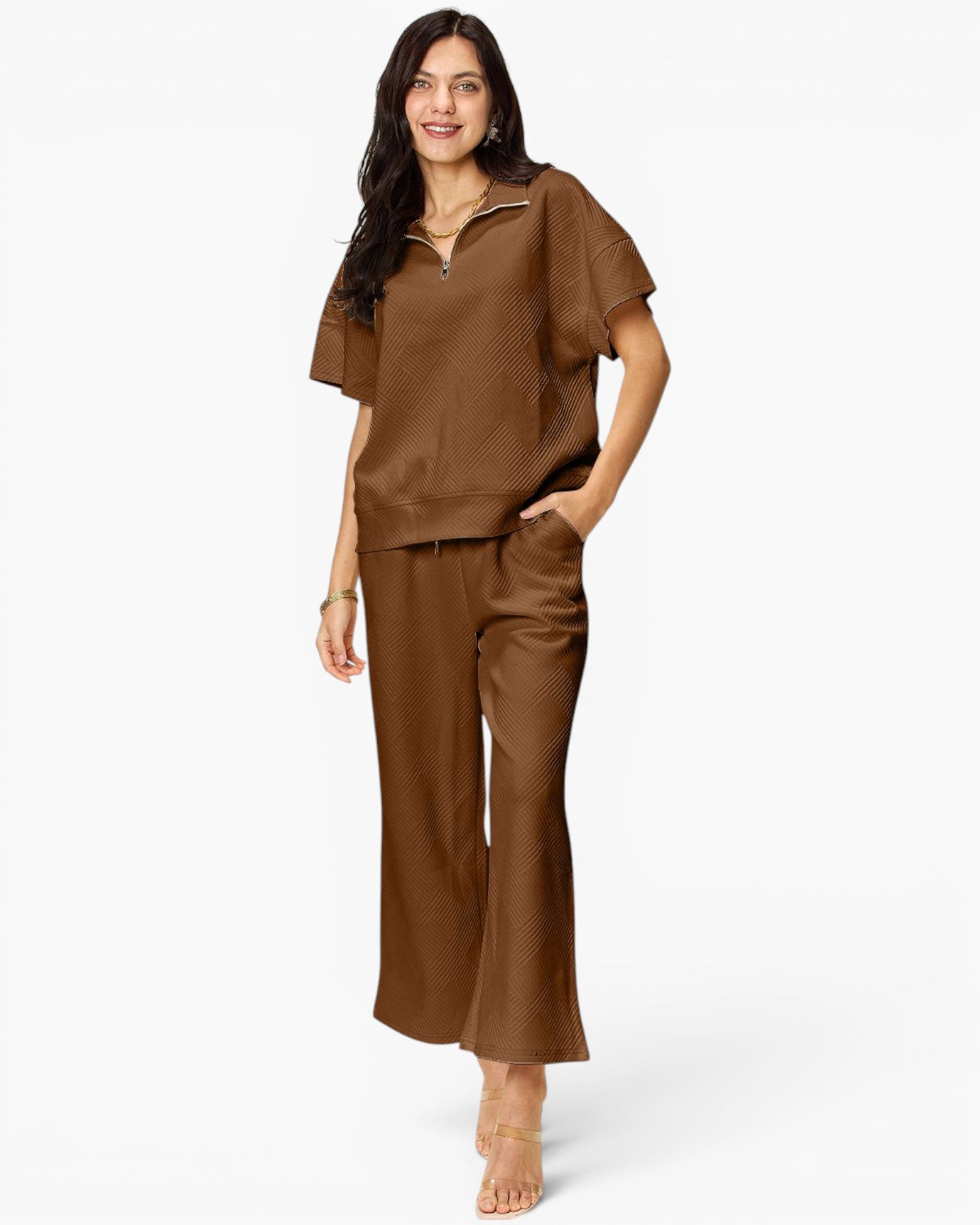 A woman modeling a matching brown lounge set consisting of a short-sleeve half-zip pullover and wide-leg pants, photographed against a clean white studio background.